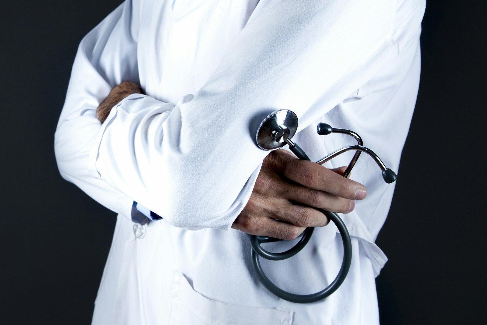 Doctor in a white coat holding a stethoscope, arms folded, face not shown
