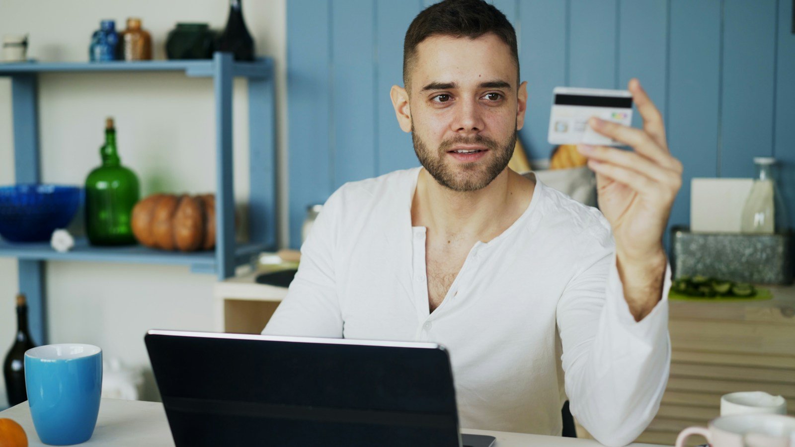 Man holding a bank card up while looking at a laptop, about to pay online