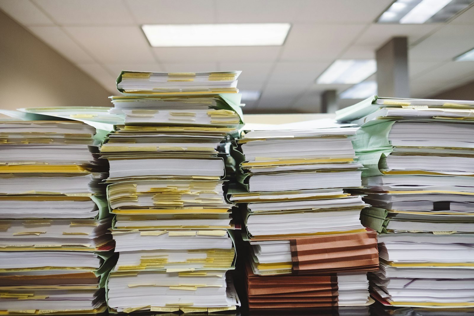 Tall stacks of paper files with tabbed pages on an office desk